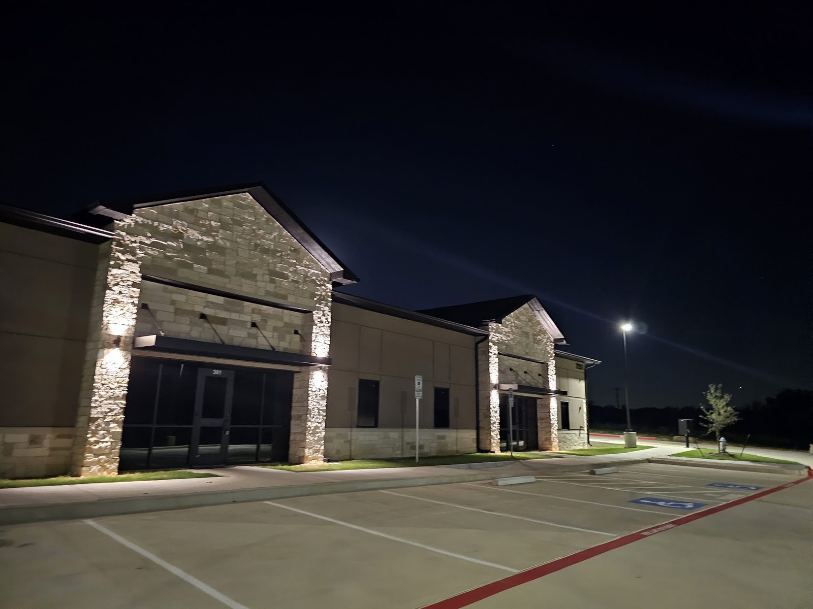 Commercial building facade and parking lot lit at night by exterior and site lighting